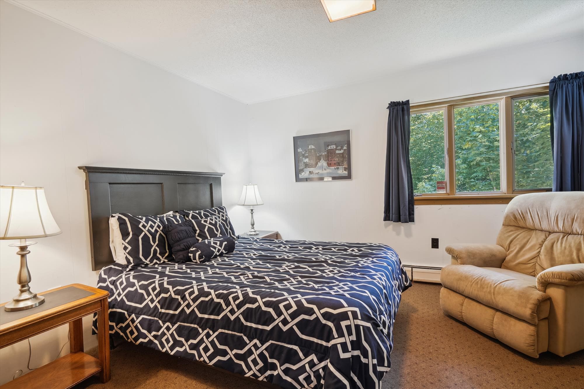 This bedroom has a queen bed and a comfortable chair.