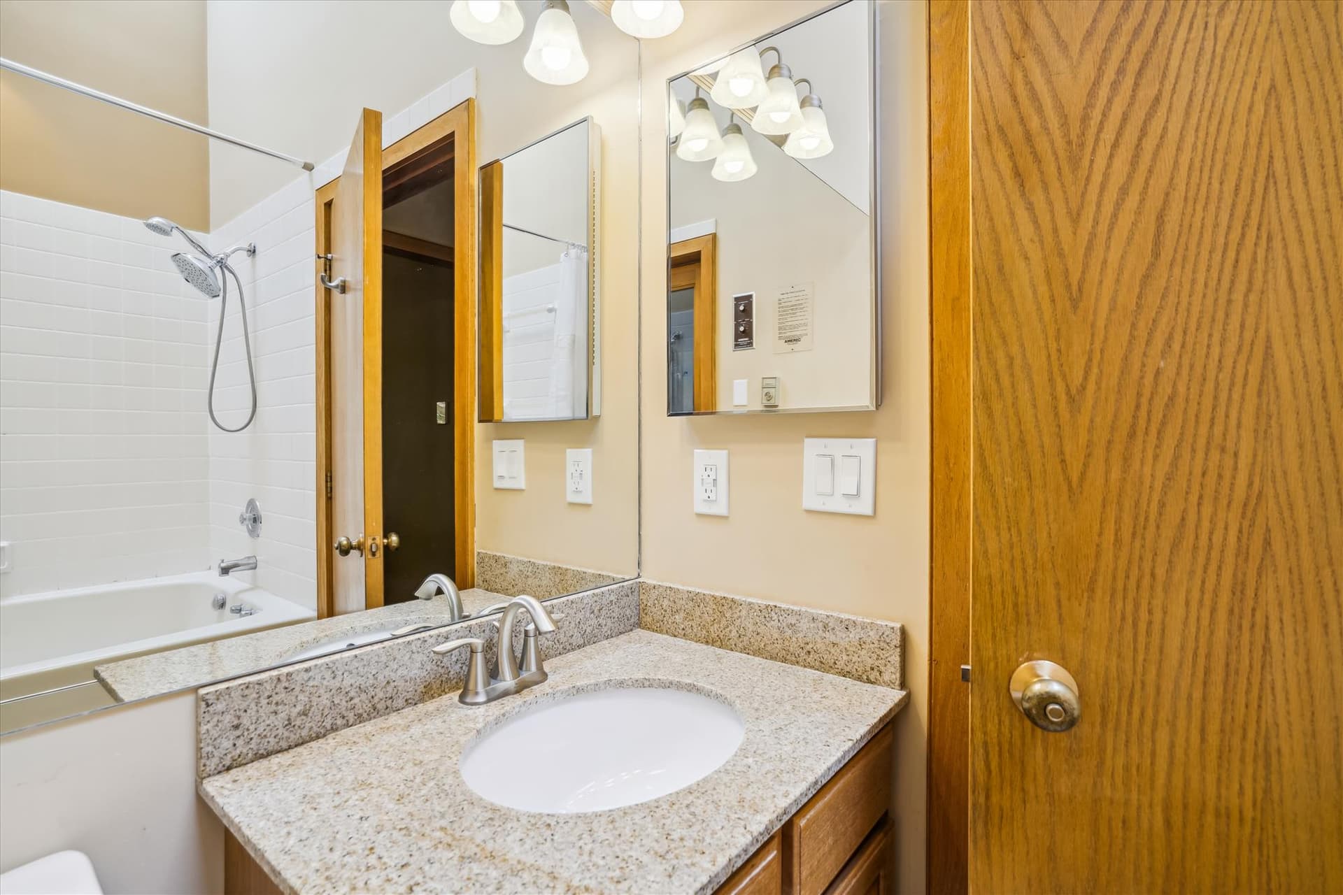 Full bathroom with granite vanity, mirror, and bright lighting.