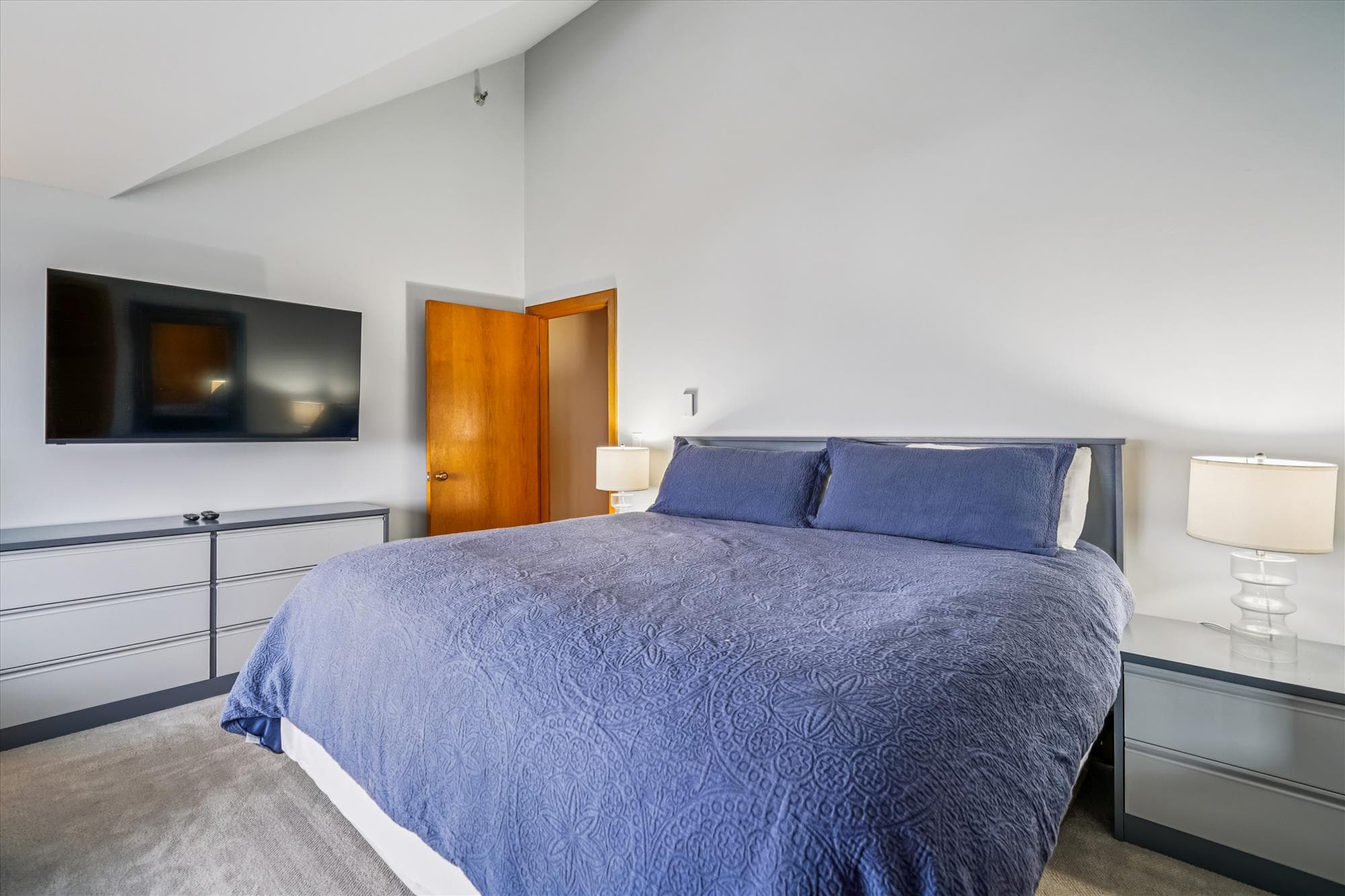 Primary bedroom with king bed, bedside lighting, dresser storage, and a mounted flat-screen TV.