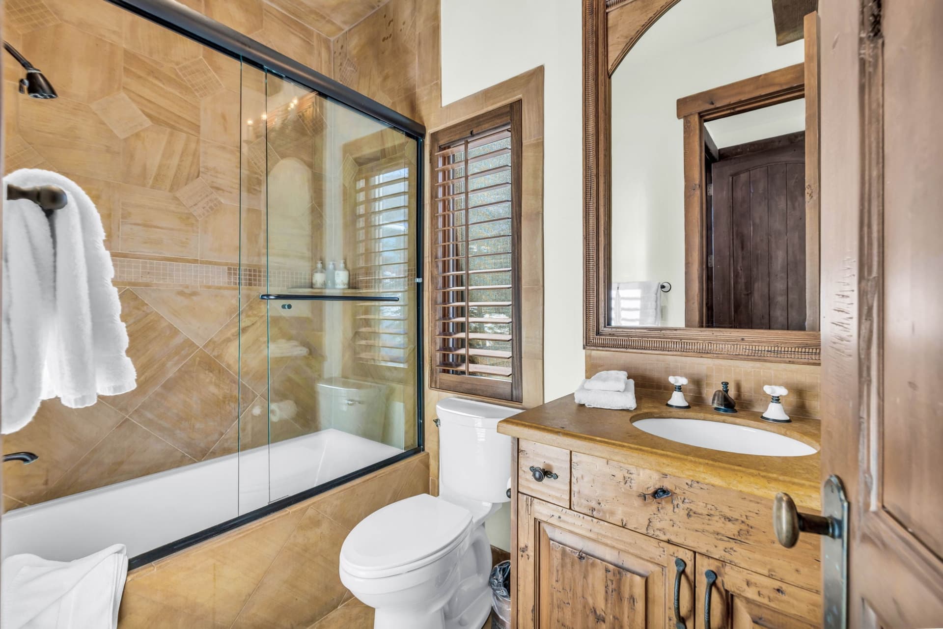 Bathroom with glass-enclosed shower, wood vanity, and rustic stone details.