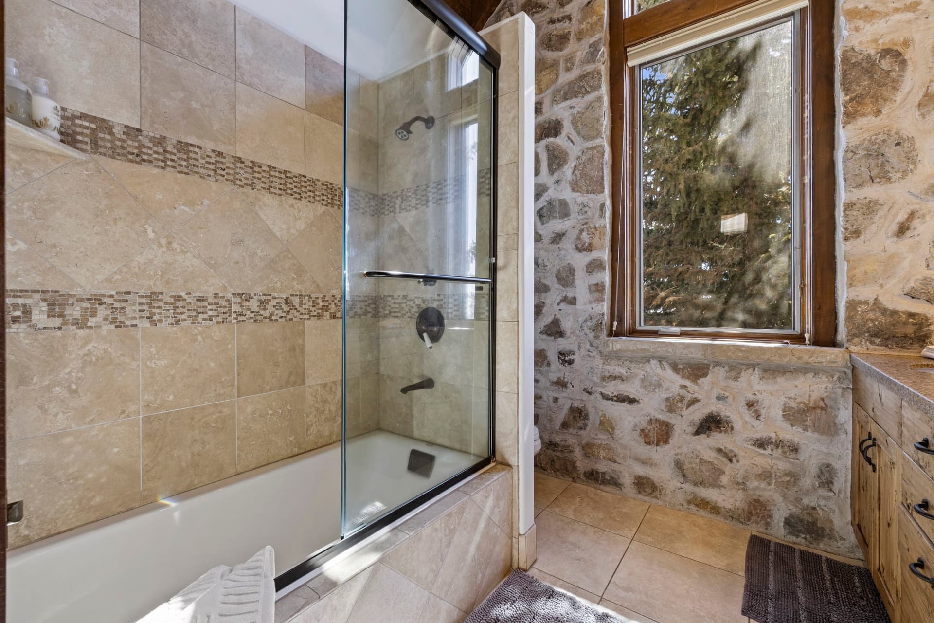 Bathroom with glass-enclosed shower, stone walls, and window with natural light.