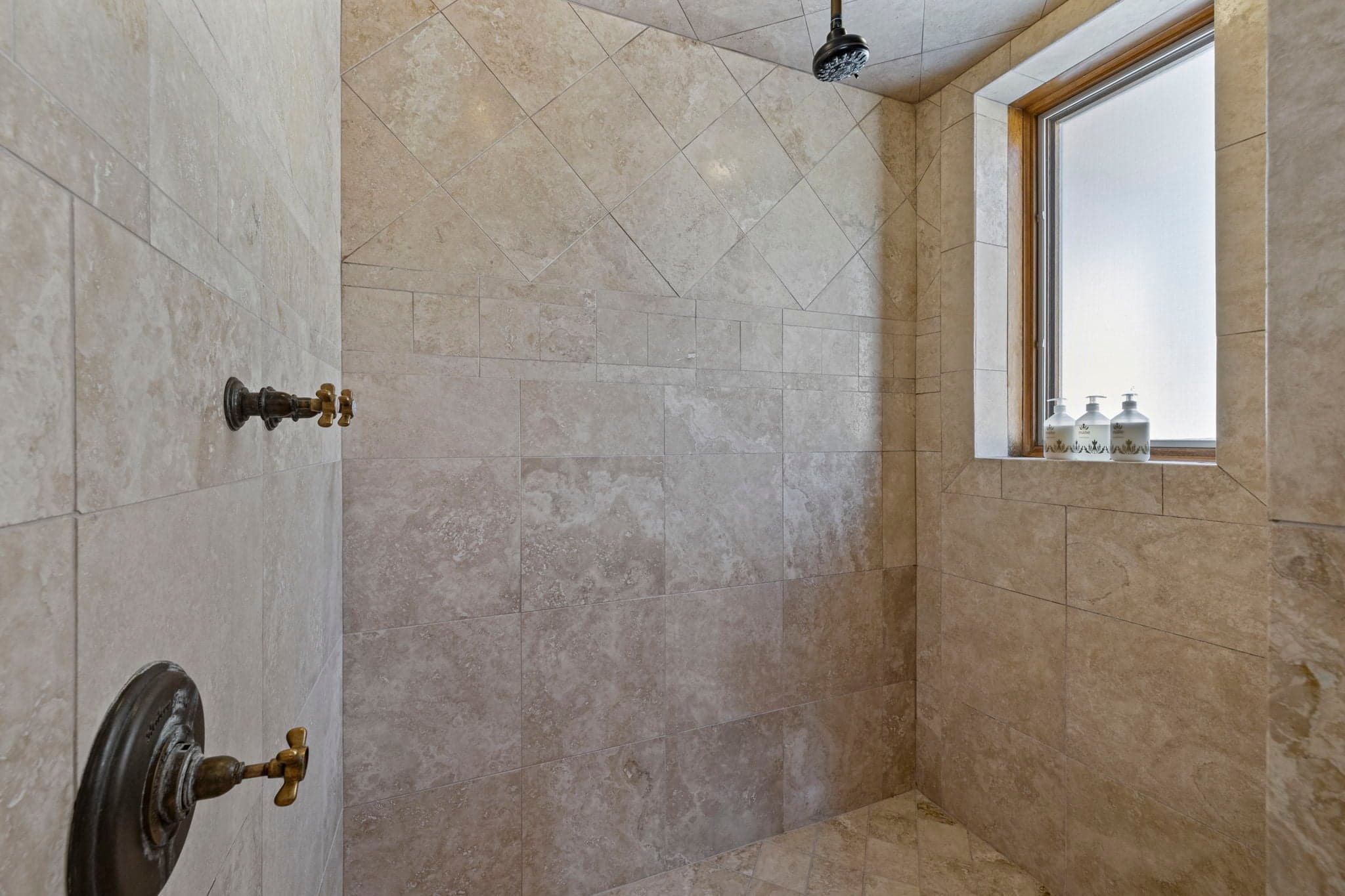 Walk-in shower with stone tile walls and rainfall showerhead.