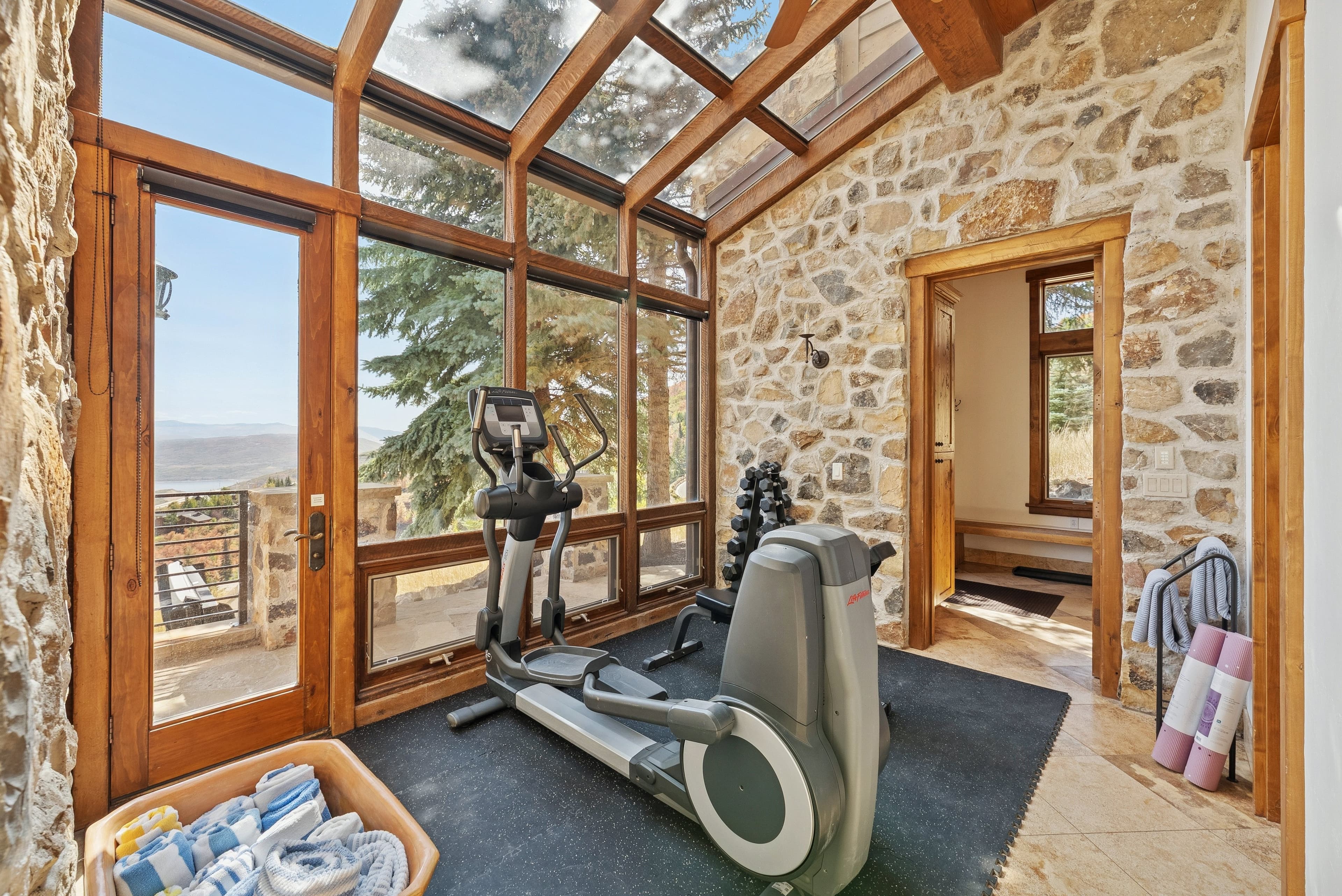 Home gym with exercise equipment in a sunlit glass-enclosed room.