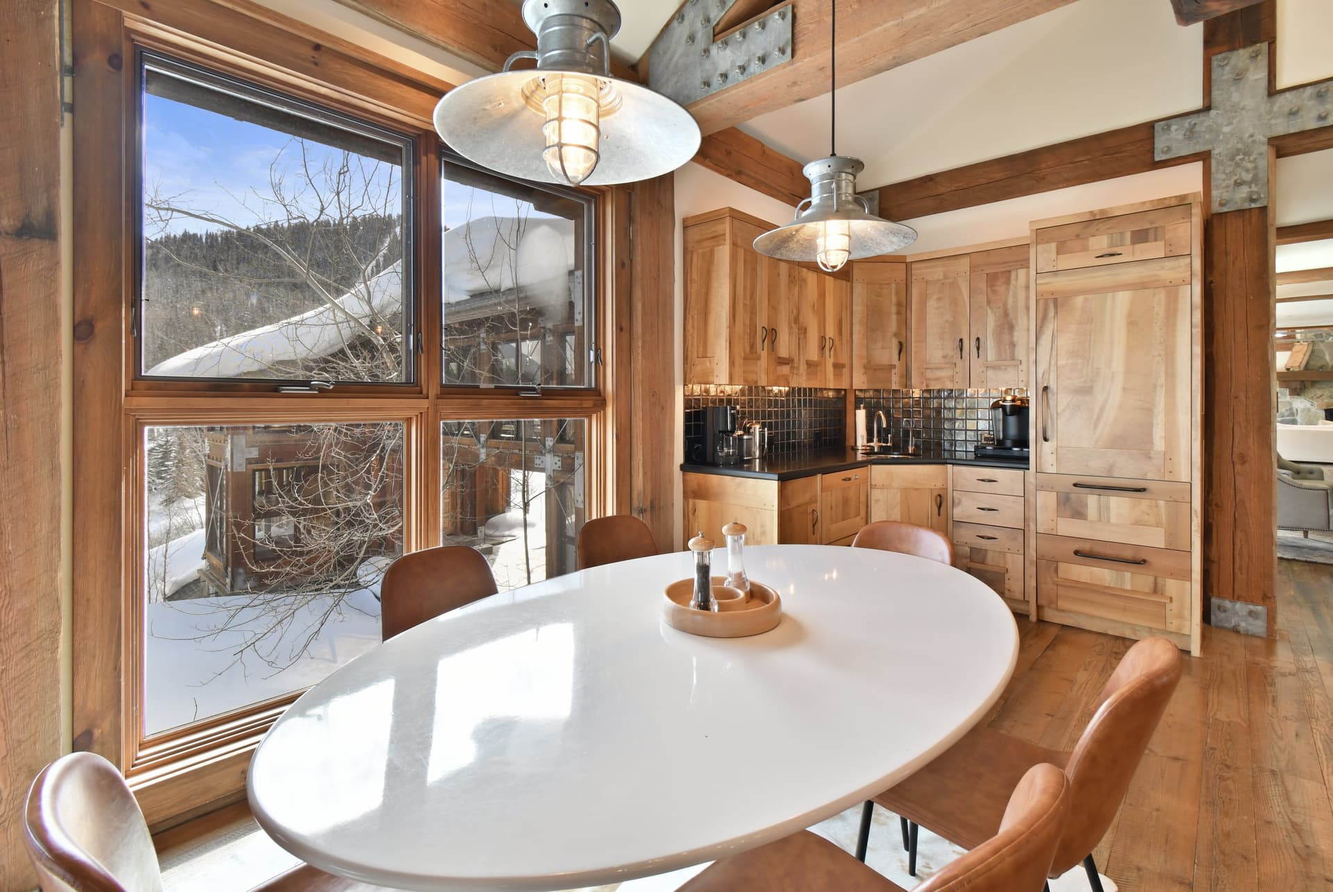 The dining table of the kitchen, with the wet bar visible in the background and a window to a snowy outdoors.