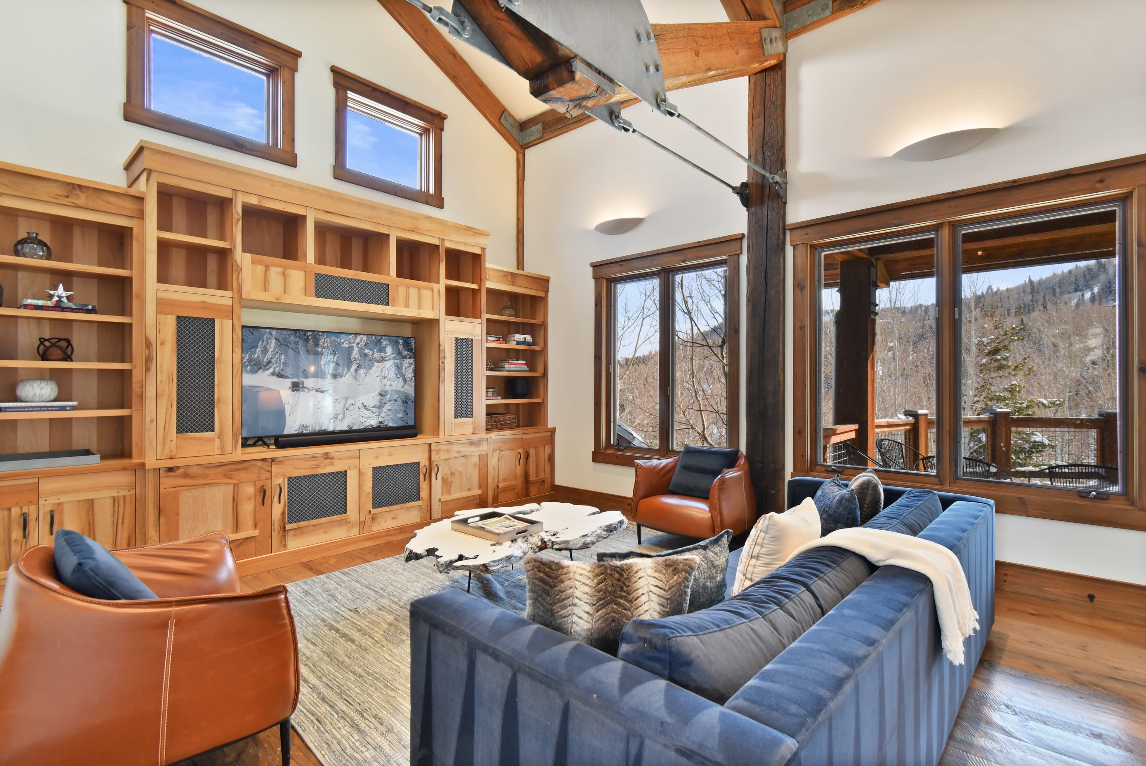 A blue couch sits in front of the ornate entertainment center of a living area, flanked by two leather armchairs.