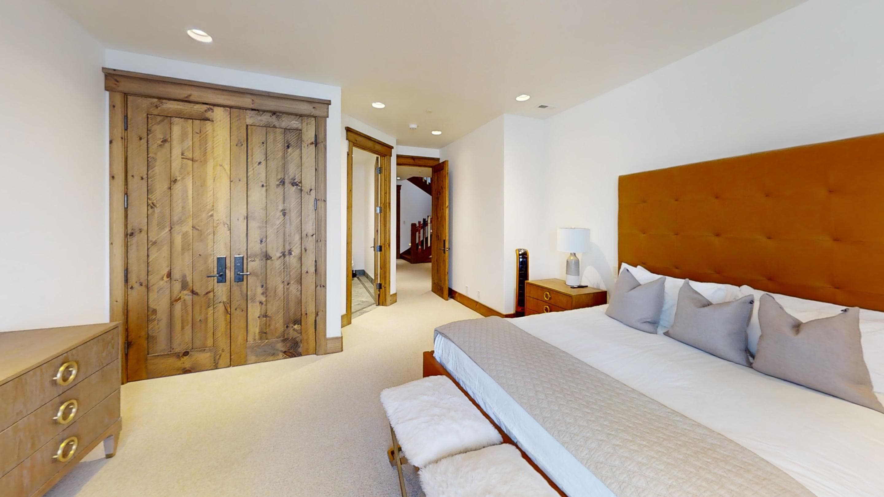 Another view of a bedroom with a red orange bedframe, showing the wooden doors of the closet and the exit doors.