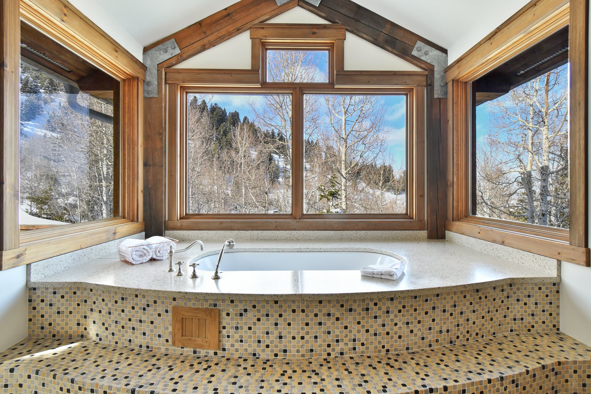 A large tub in front of multiple windows, surrounded and decorated by black and white checkered tiles.