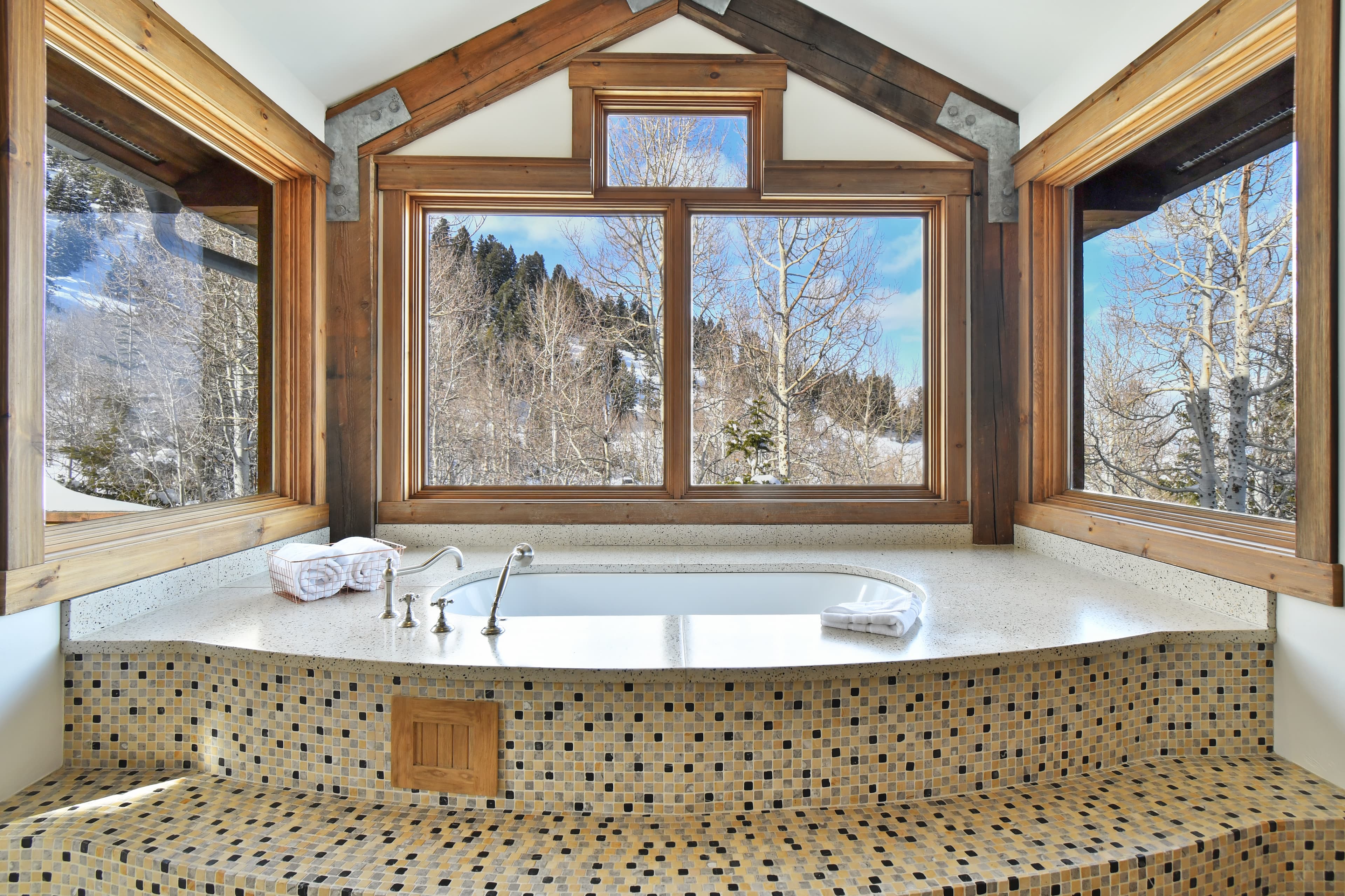 A large tub in front of multiple windows, surrounded and decorated by black and white checkered tiles.