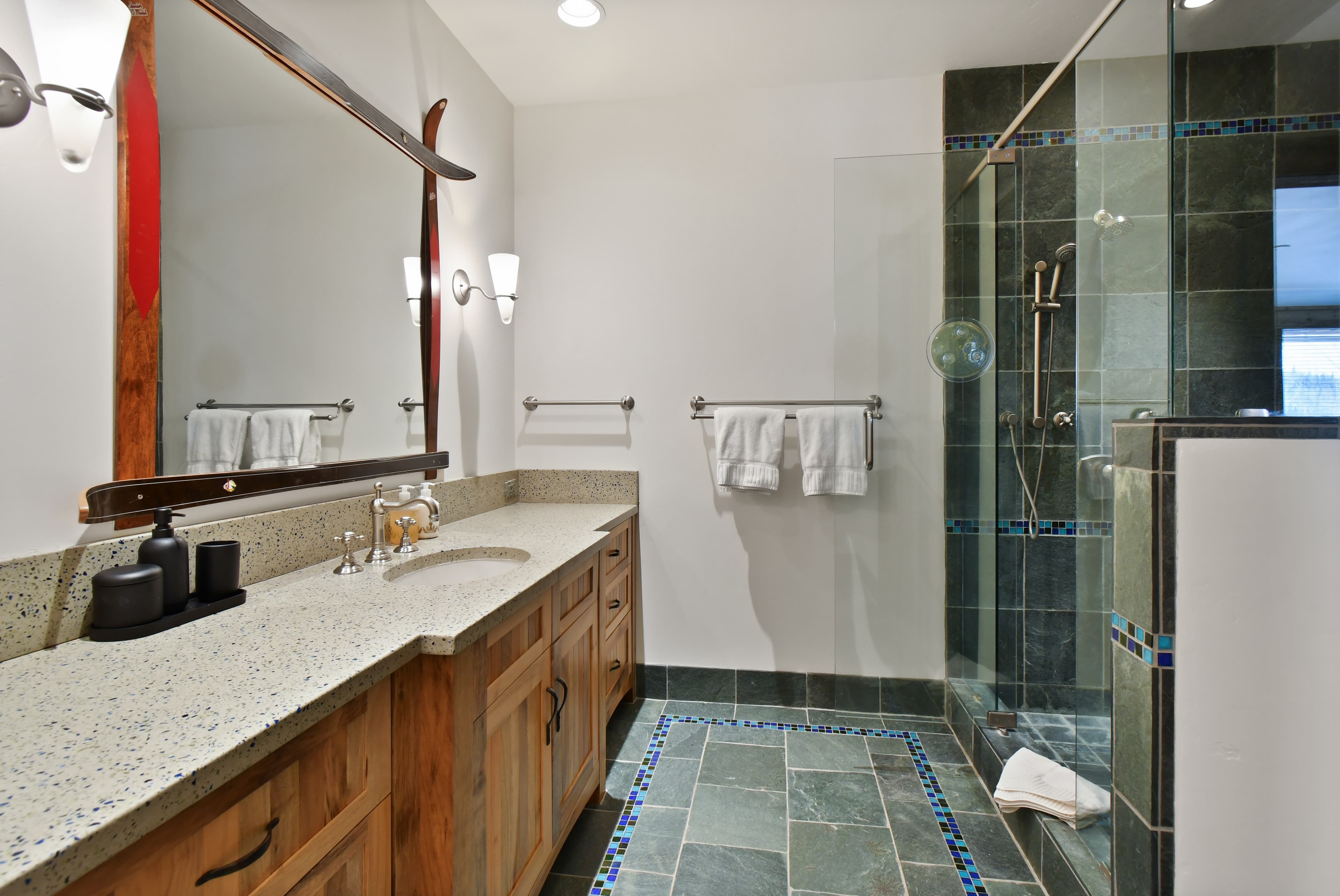 A simple sink sits in a long counter in front of a wall mirror, with a walk-in shower on the other wall.