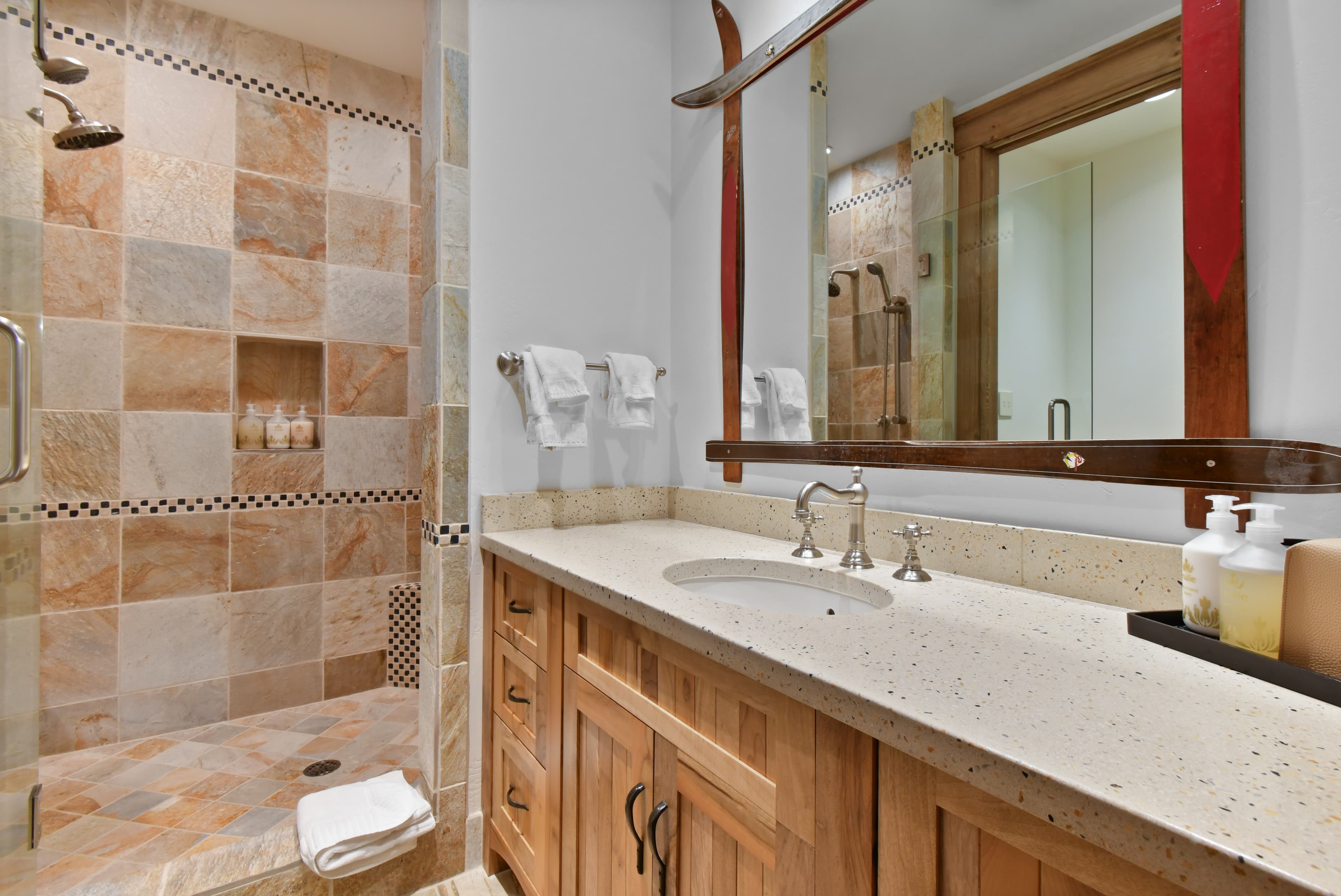 Brown decorative tiles line the walls of a walk-in shower, next to a simple sink/mirror combo.