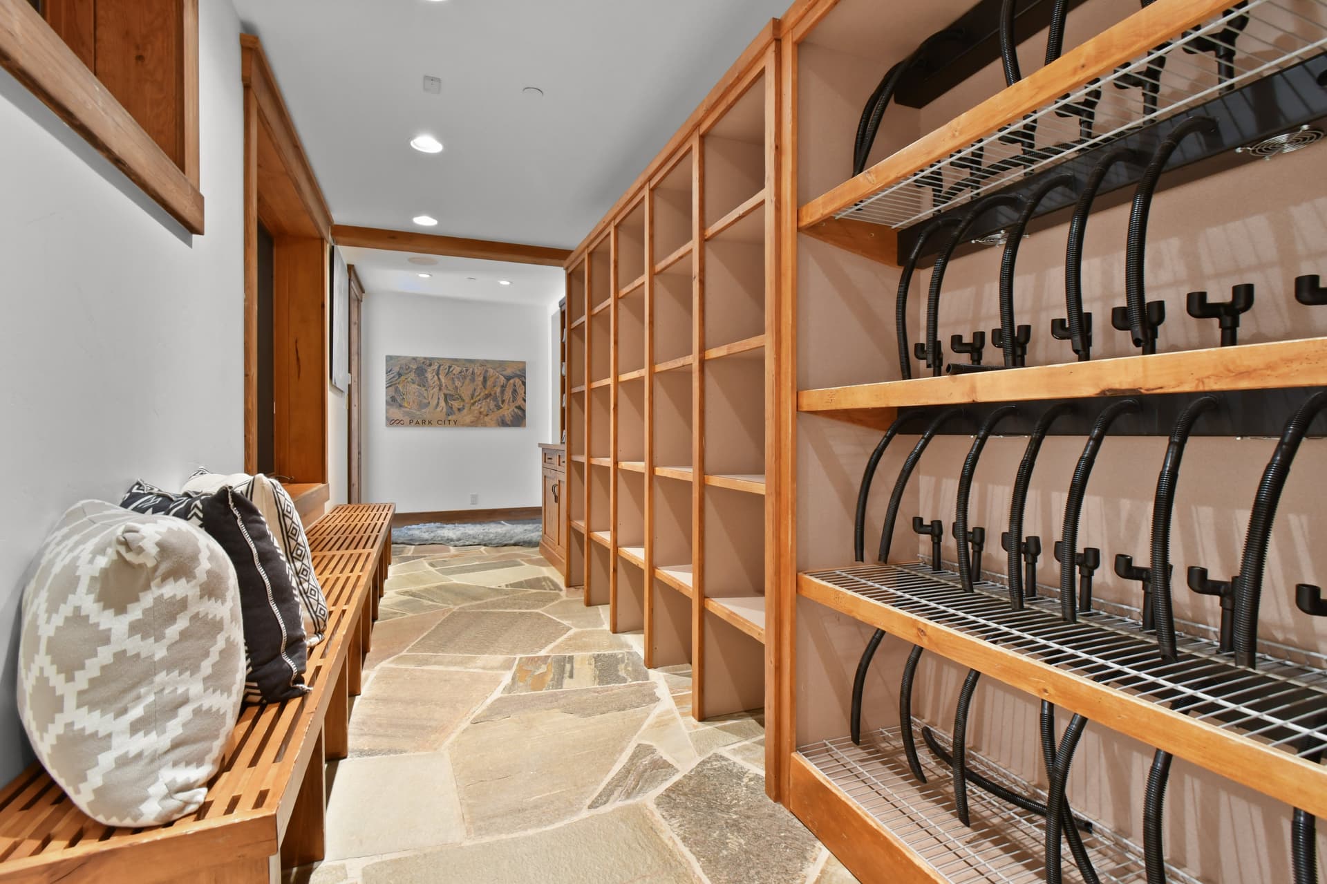 Racks and shelves line one of the walls of the ski closet, with a bench and cushions on the other wall.