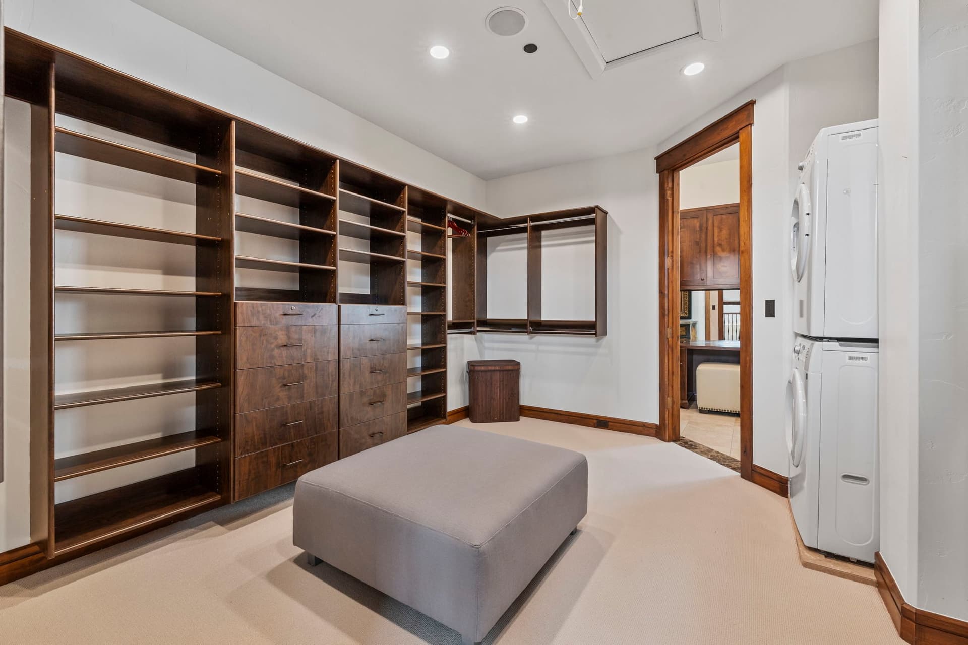 large walk in primary closet with an ottoman in the center