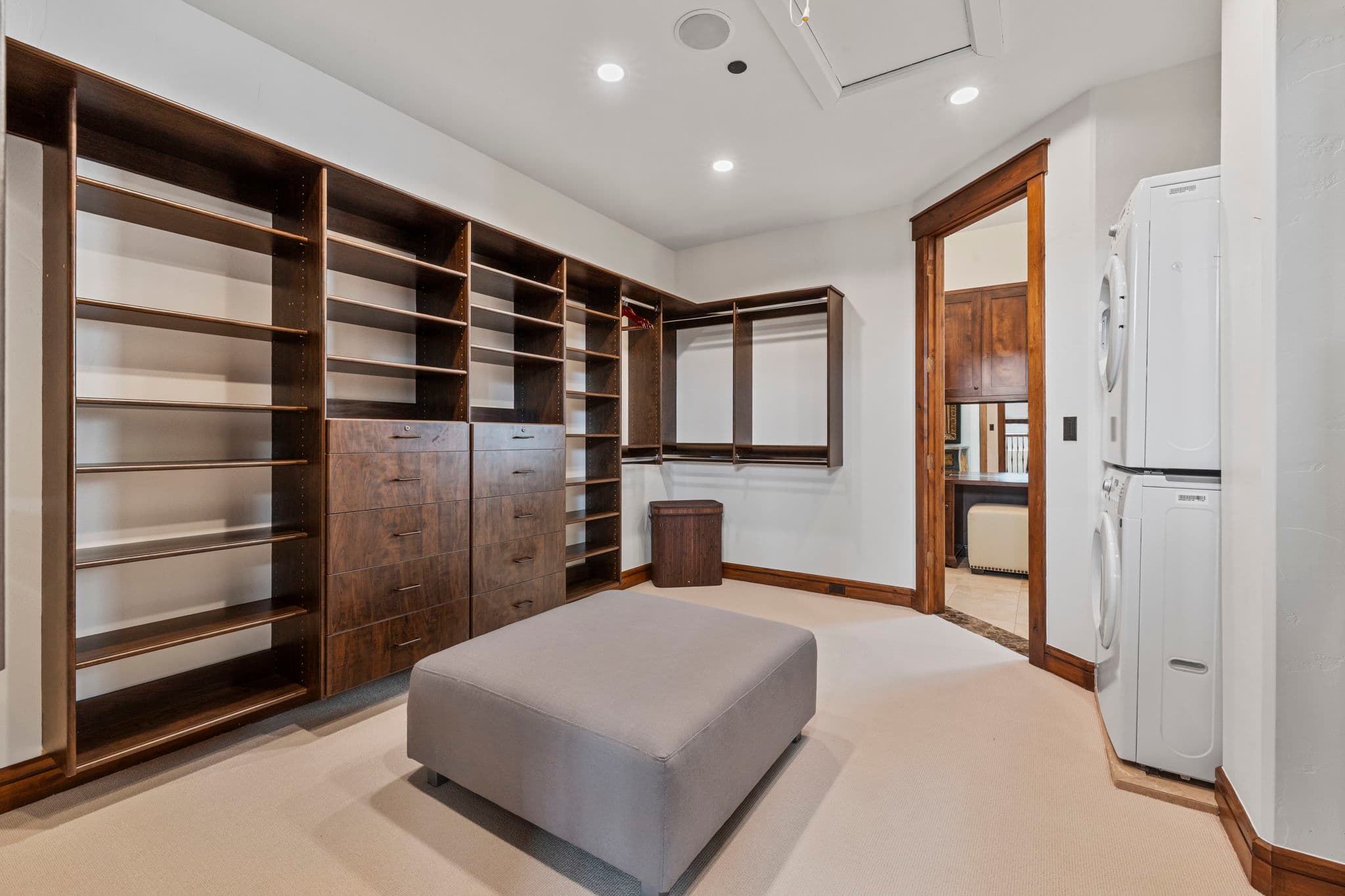 large walk in primary closet with an ottoman in the center