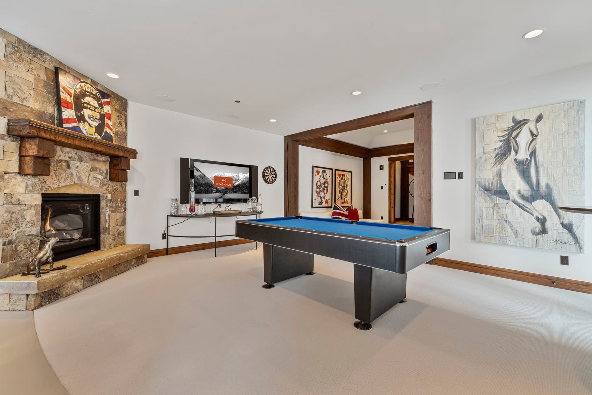 a large stone fireplace in the game room with TV and pool table. The TV has Luxe Haus displayed on the screen